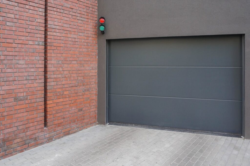 Commercial garage door with modern design, red and green traffic lights, brick wall, and paved surface, relevant to installation services in Kelowna by Vision Overhead Doors.
