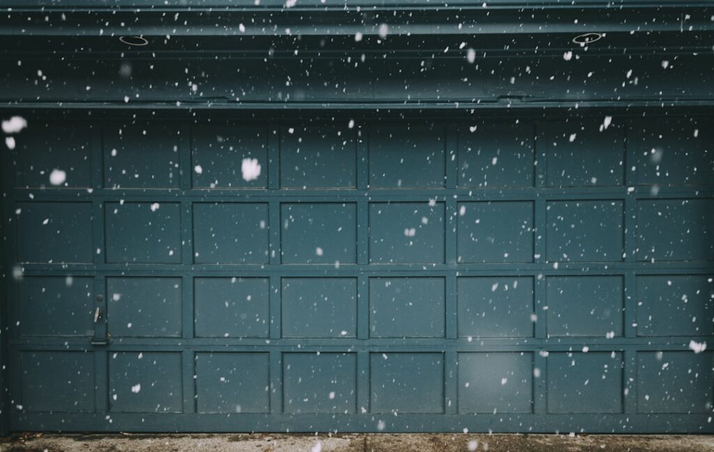 Garage door with a blue exterior during snowfall, illustrating winter conditions relevant to garage door opener selection for cold climates.